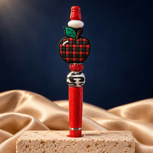 Red glitter-look apple beaded pen shown upright, with a red-and-black checkered apple focal piece, green leaf, and black-and-white patterned bead