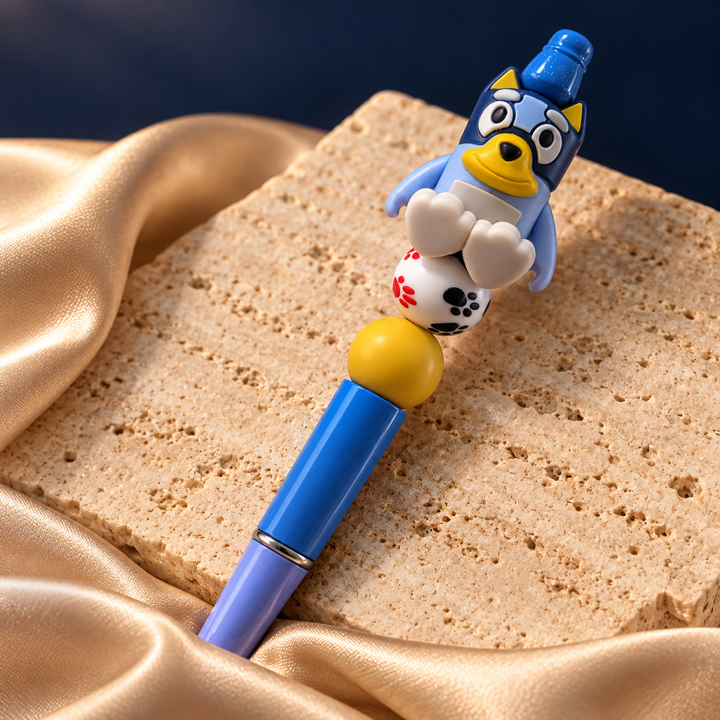 Blue puppy beaded pen with a yellow muzzle, white paw-print bead, yellow accent bead, and glossy blue barrel, resting on stone