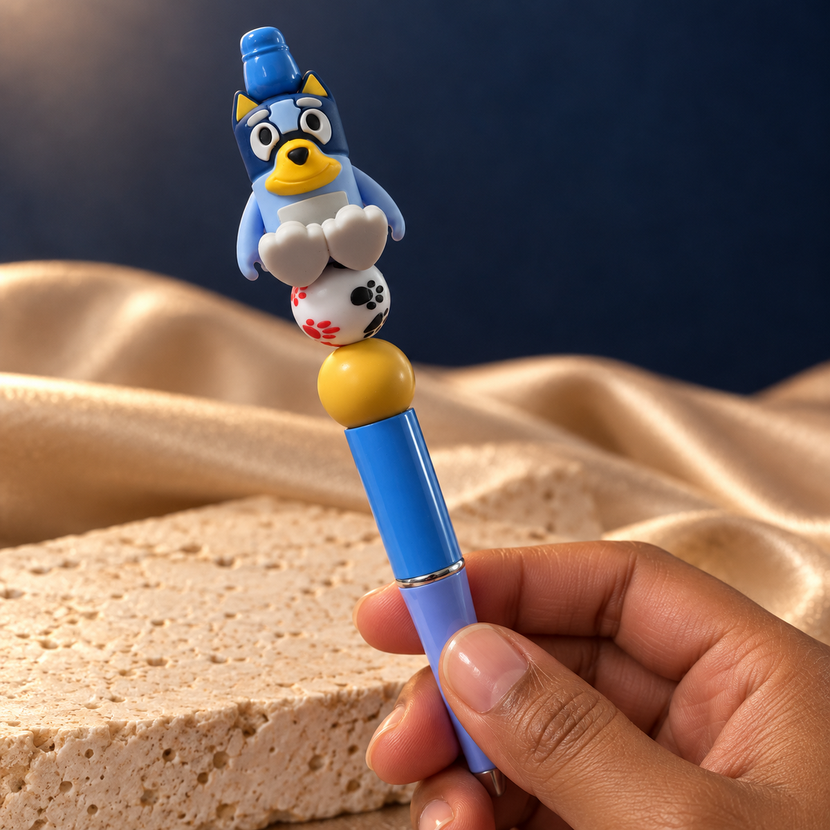 Blue puppy beaded pen held in hand, showing its white paw-print bead, yellow accent, and glossy blue barrel