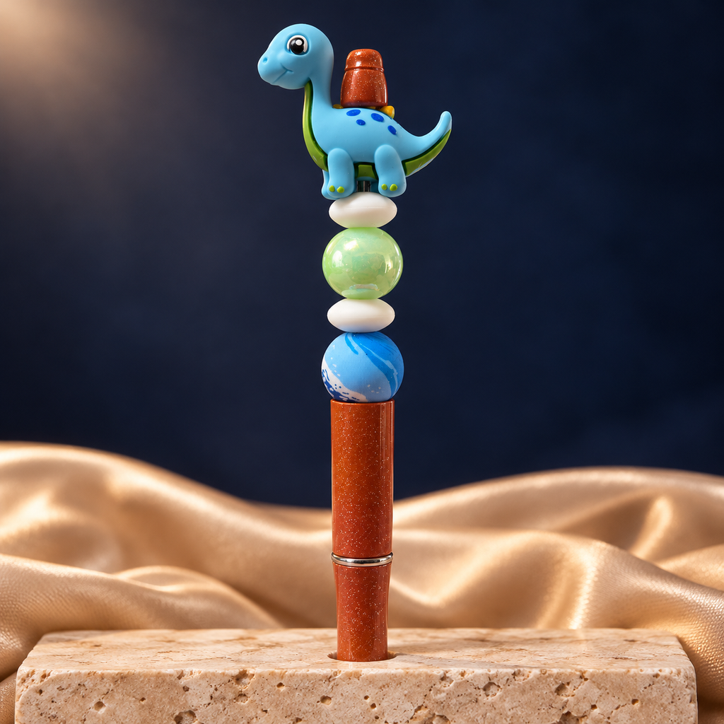 Blue dinosaur beaded pen with an orange glitter-look barrel, green and blue beads, and white spacers, shown upright