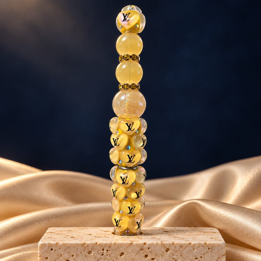 Yellow beaded pen standing upright with heart embellishments bearing black lettering, translucent yellow beads, and golden sparkling spacers