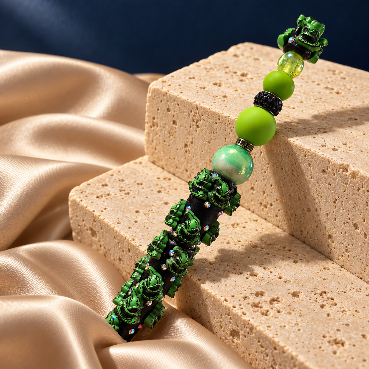 Midnight Mischief green character pen resting on stone, with lime beads and sparkling accents on a black decorated barrel