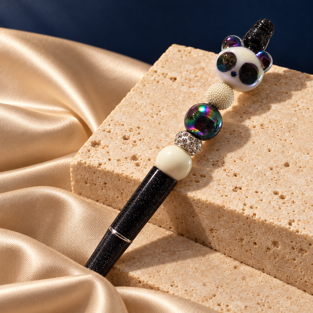 Prism Panda black glitter-look pen resting on stone, with a panda focal piece, iridescent bead, and cream-colored accents