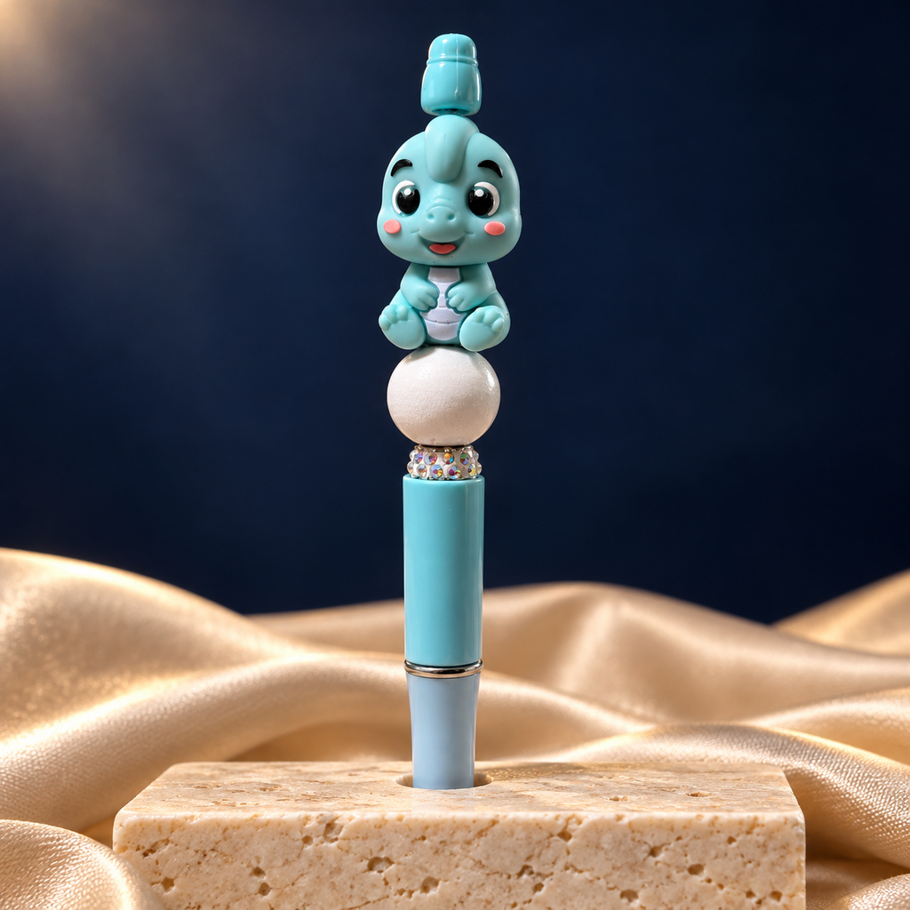 Teal baby-dinosaur beaded pen shown upright, with a white pearl-look bead, sparkling accent band, and teal and pale-blue barrel