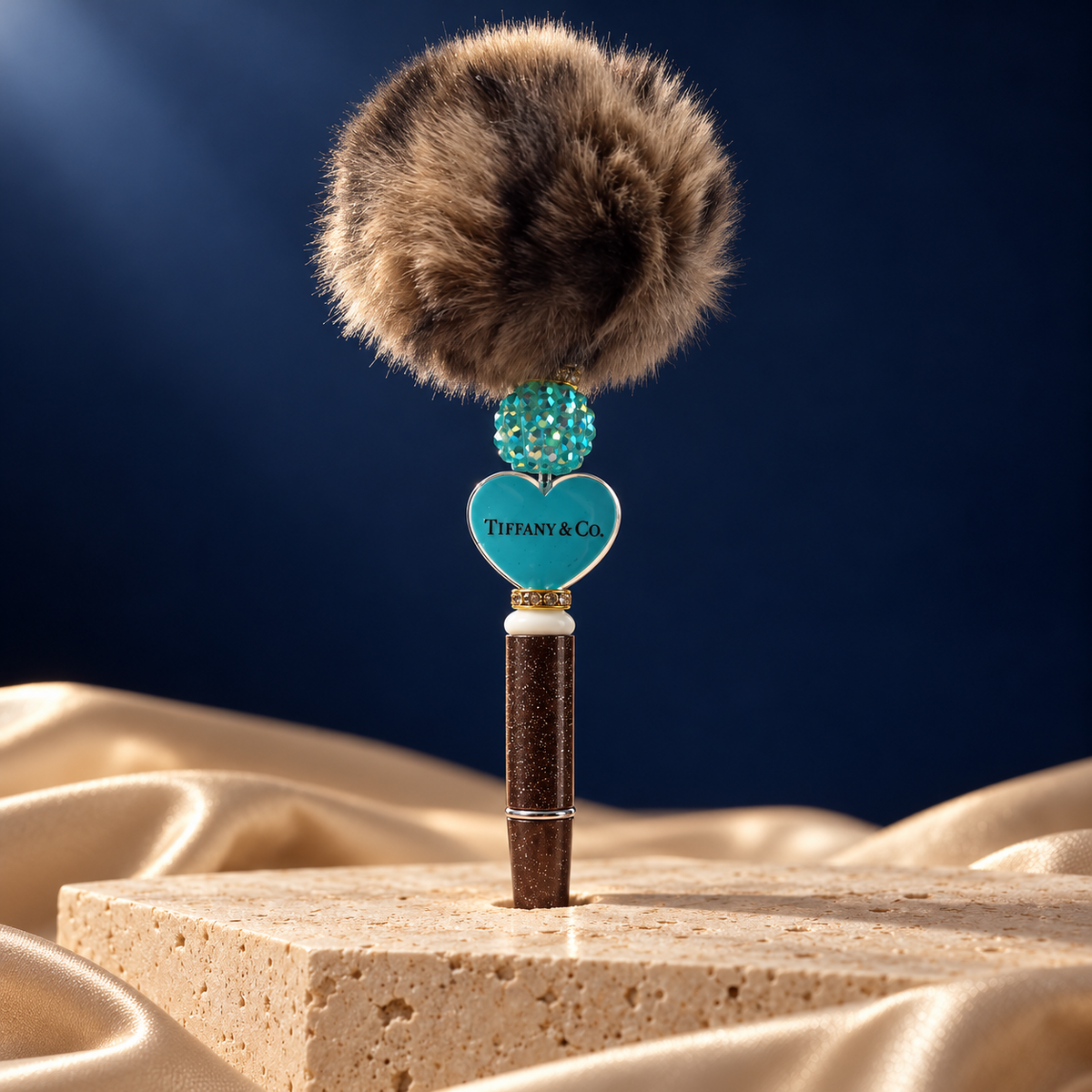 Brown glitter-look pen with a turquoise heart reading Tiffany & Co., a turquoise sparkling bead, and a brown pom-pom